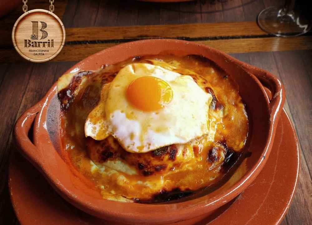 Francesinha da Pita do Barril, gratinada e servida com ovo numa travessa de barro